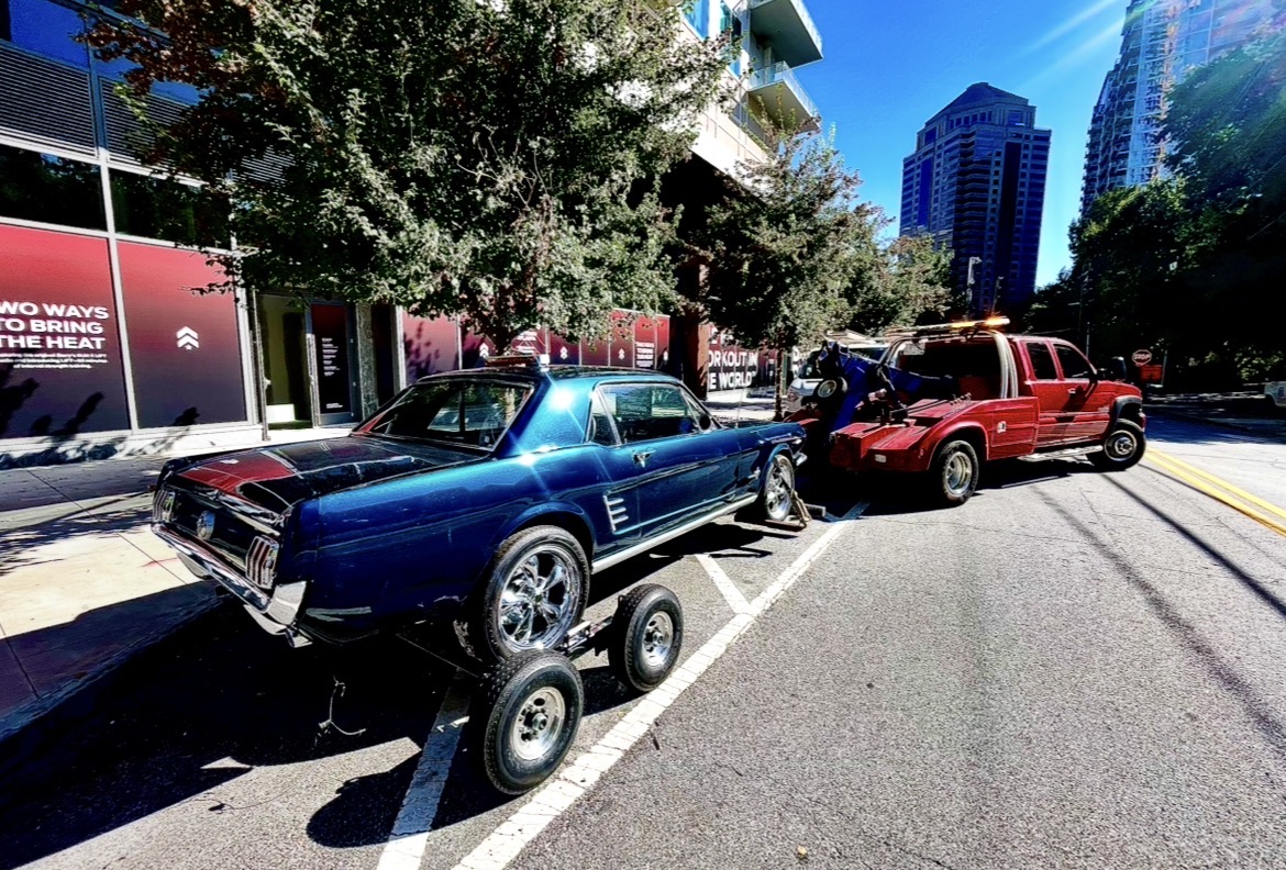 Tow truck towing a blue Mustang on a city street